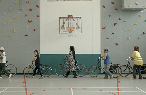 Women walk around a gym with their bicycles