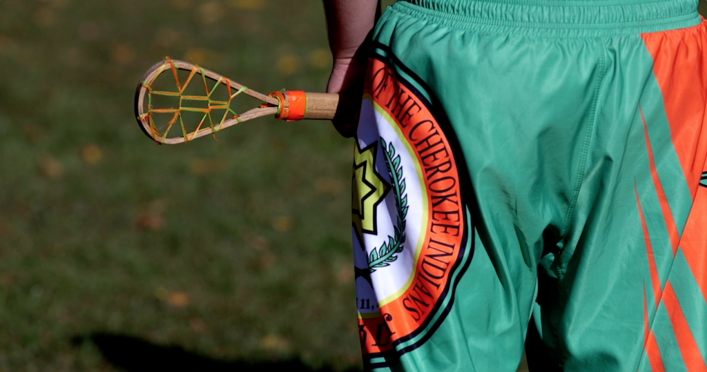 Close-up of the Eastern Band of Cherokee Indians logo on shorts and a stickball stick. Image from the short doc She Carries On.